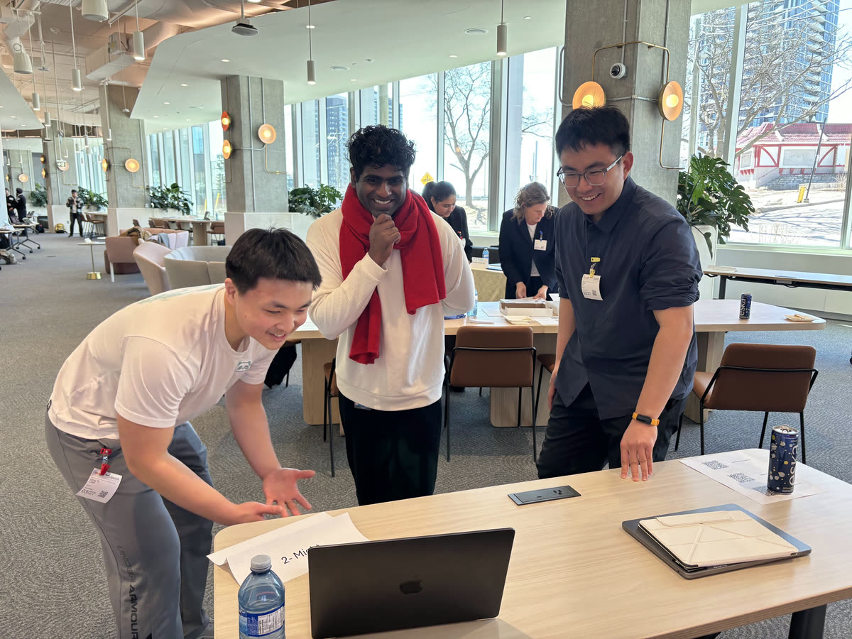 Three students laughing together as they demo their prototype on a laptop at Google’s Kitchener office.